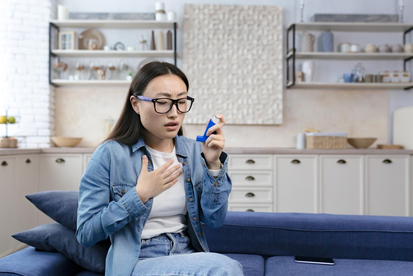 A woman is sitting on a couch using an inhaler.