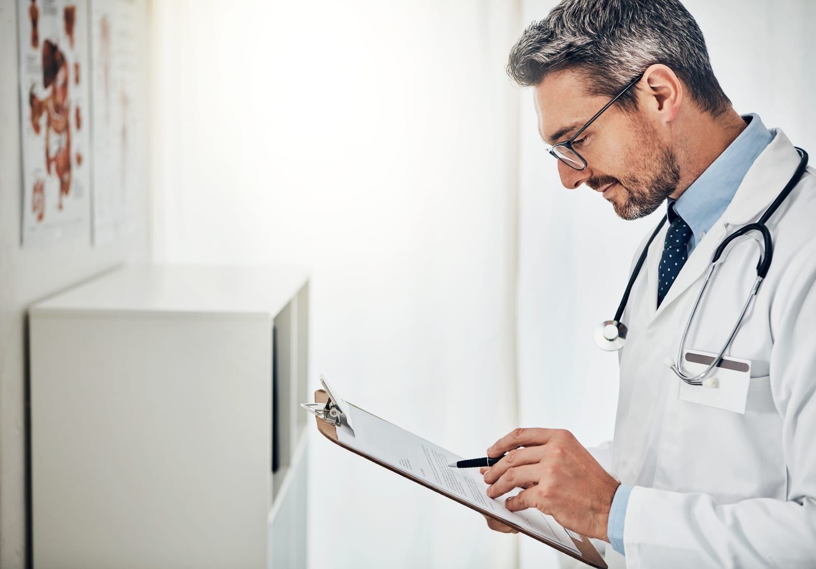 A doctor reading a patient file while standing in his consultation room.