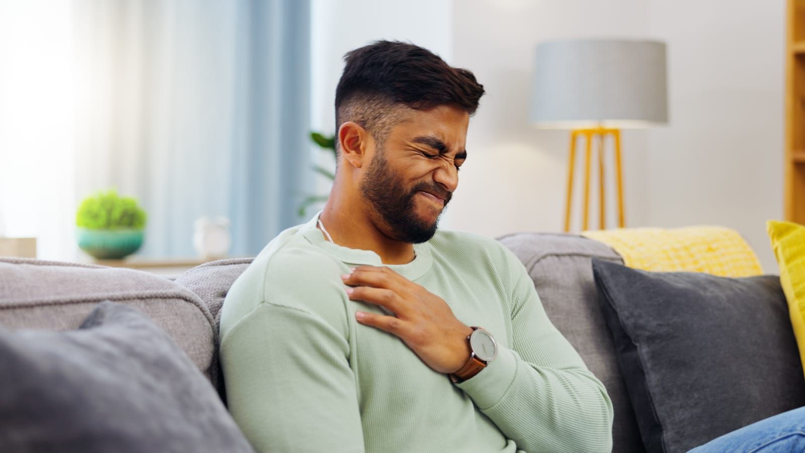 A man is sitting on a couch holding his chest in pain due to GERD.