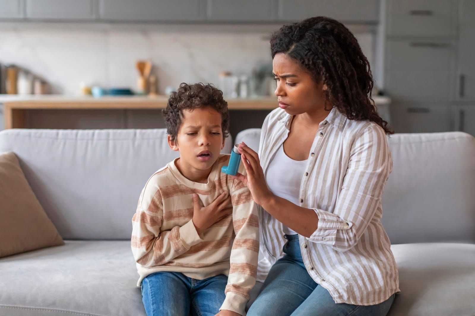 Caring mother giving blue asthma inhaler to her sick son at home.