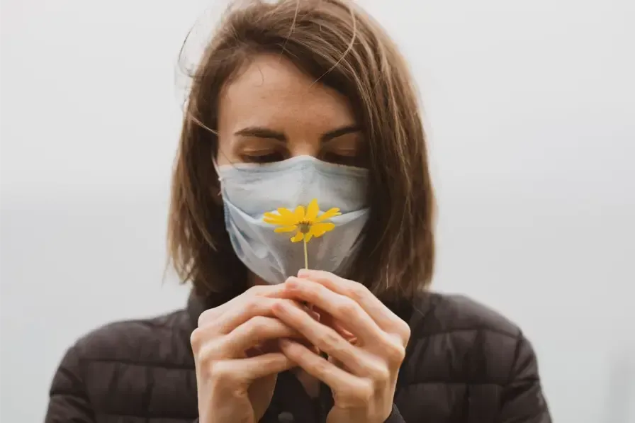 Woman in a face mask holding a flower to her nose, illustrating smell loss from chronic sinusitis.