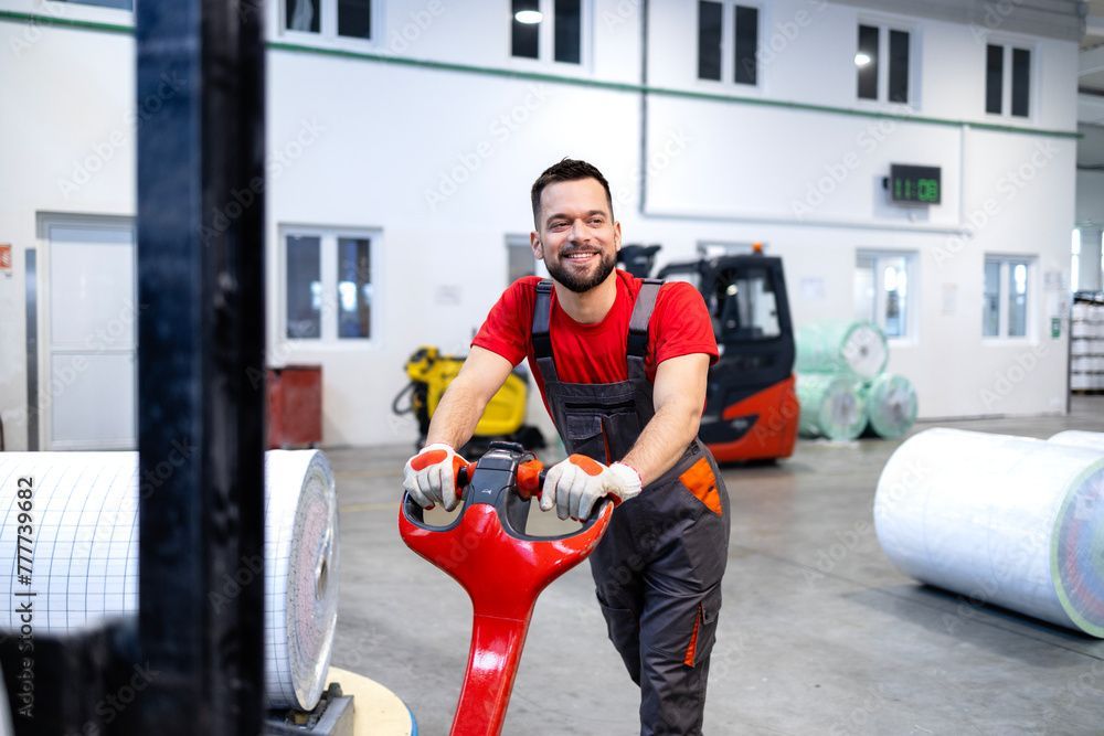 Warehouse worker smiling while operating a pallet jack, surrounded by rolls of paper.