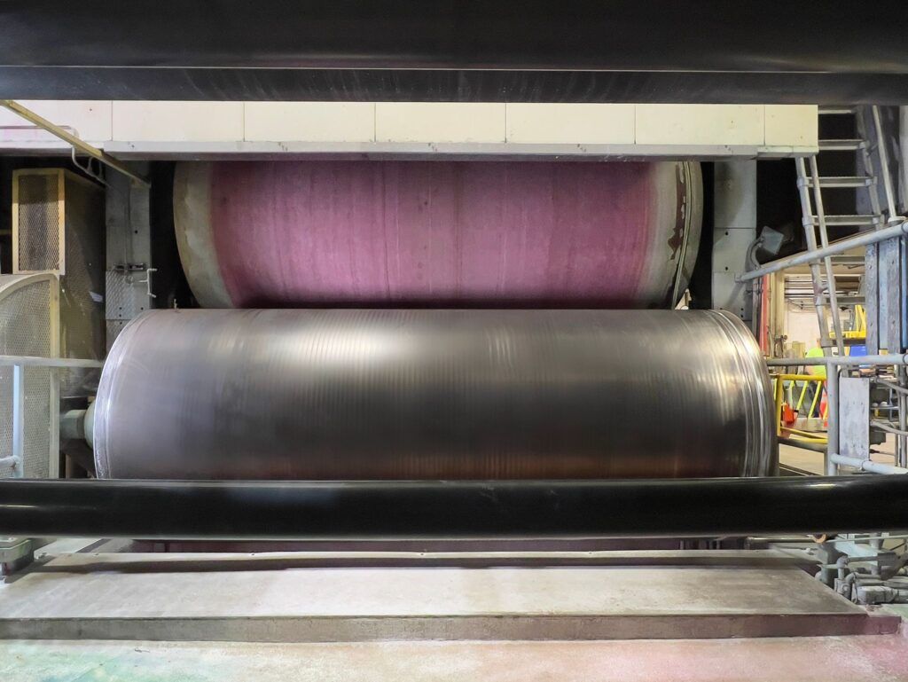 Large industrial paper press with a pink roller over a silver roller.