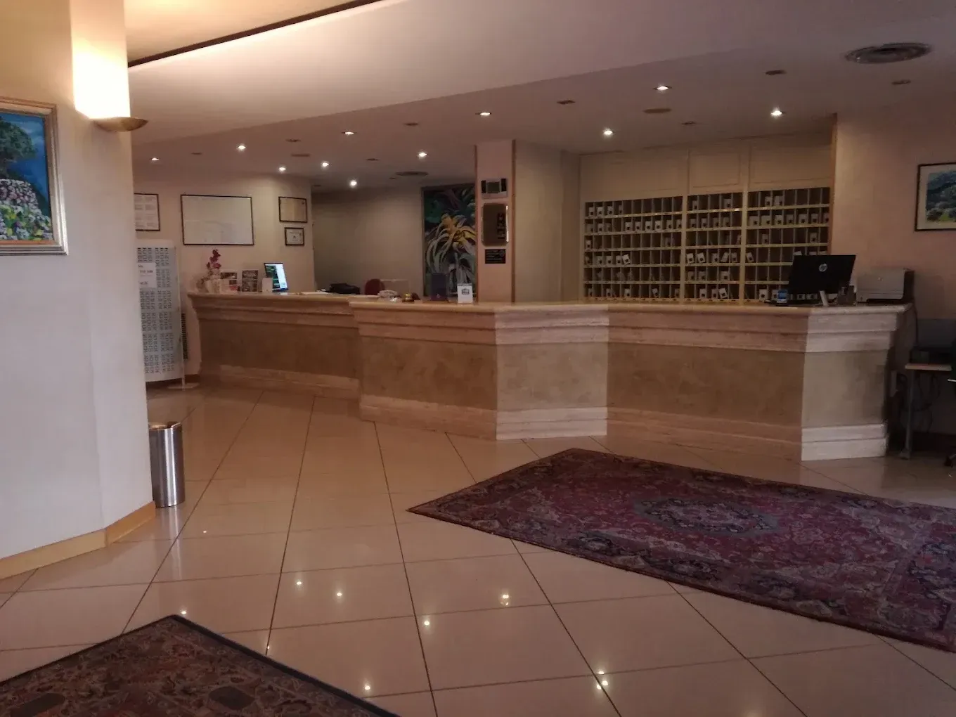 Il bancone della reception di un hotel, con un piano d'appoggio chiaro e dalle forme poligonali e una griglia di scomparti per la posta sulla parete.