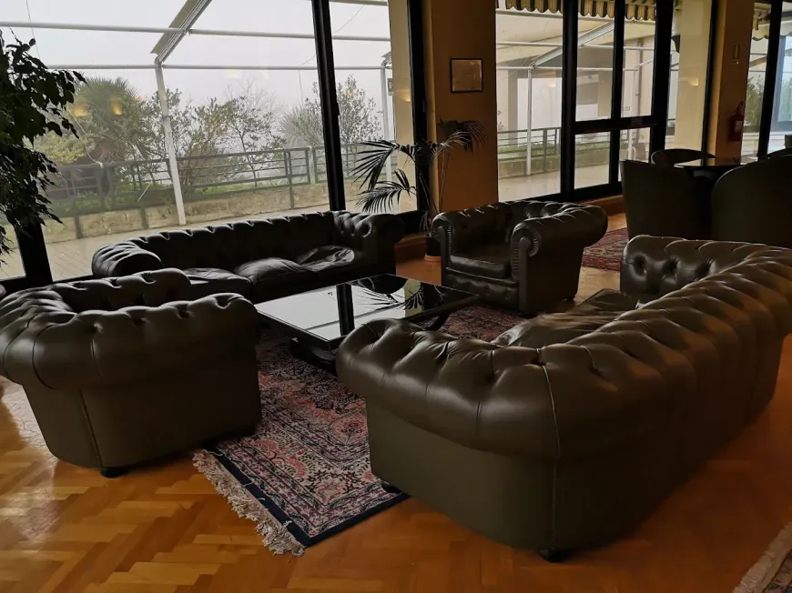Una zona lounge con divani Chesterfield in pelle scura e una poltrona disposti attorno a un tavolino di vetro su un tappeto a motivi geometrici.