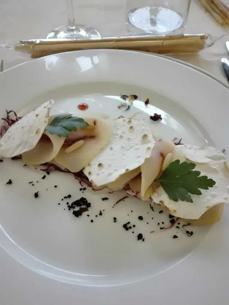 Un antipasto servito al piatto con sottili fette di pesce guarnite con cracker croccanti, prezzemolo fresco e un mix di erbe aromatiche scure.