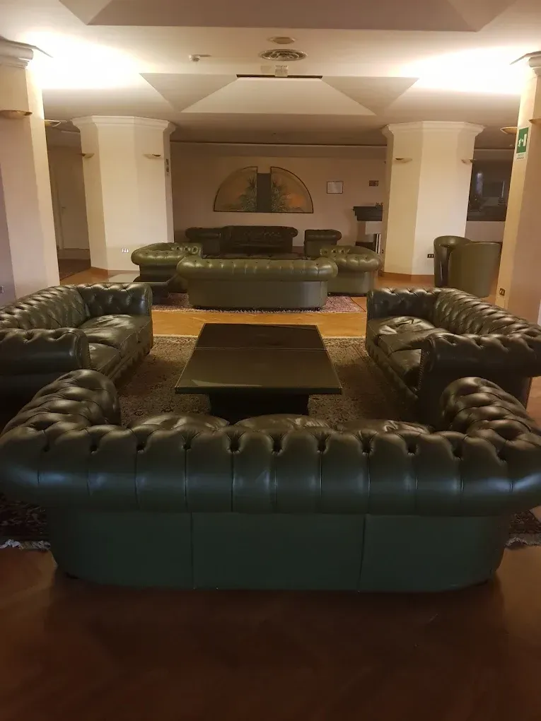 Una sala d'attesa con divani in pelle verde scuro disposti attorno a un tavolino da caffè, con una decorazione murale a motivi sullo sfondo.
