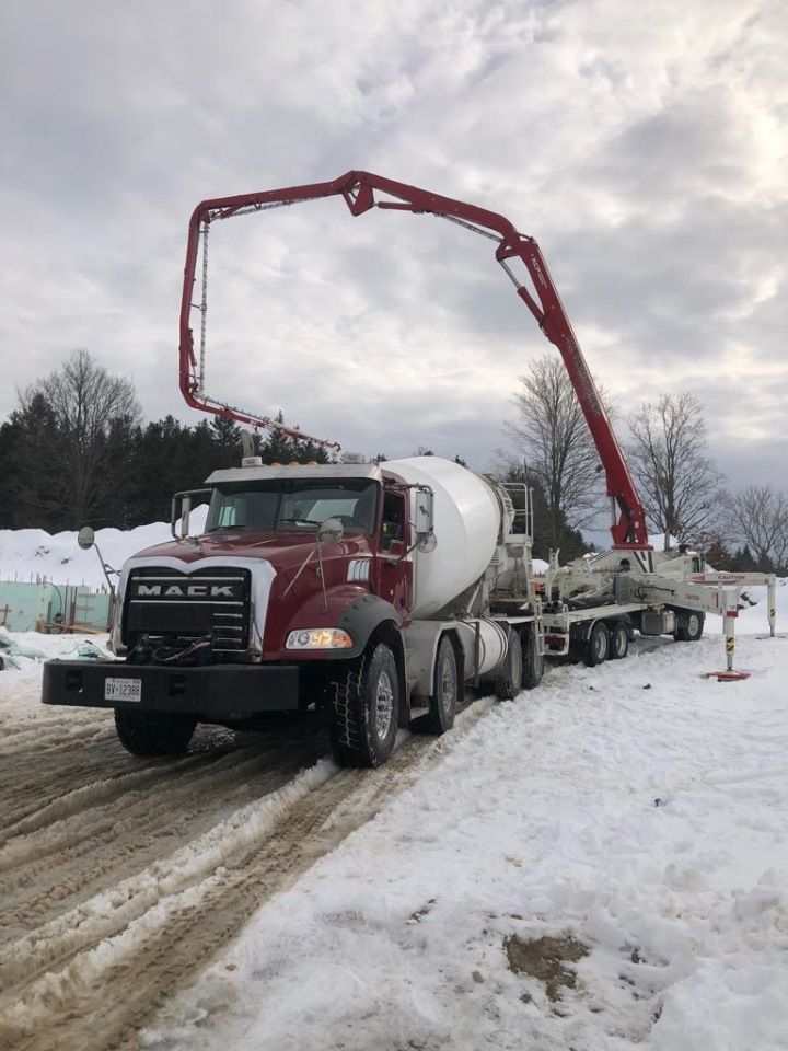 A concrete mixer truck is driving down a snowy road.