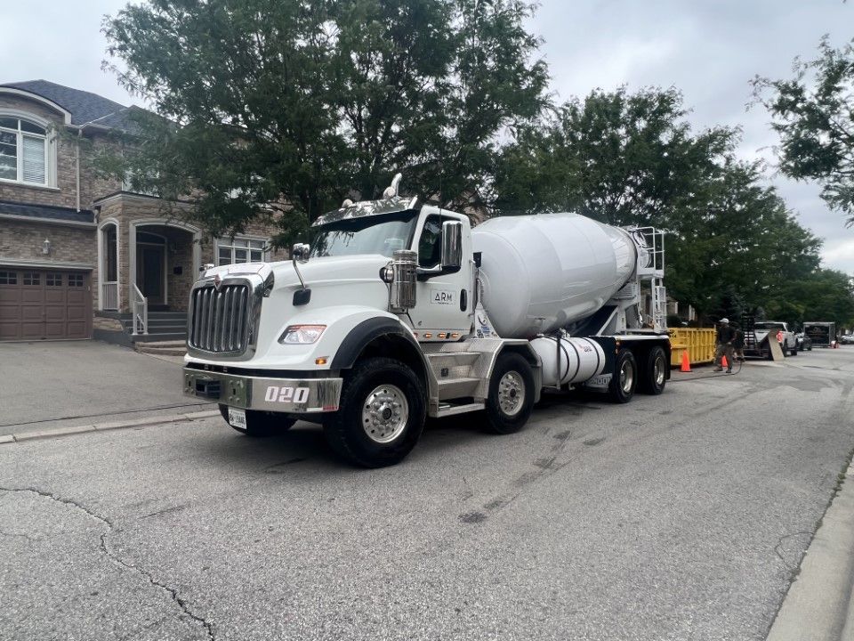 A concrete mixer truck is parked on the side of the road in front of a house.