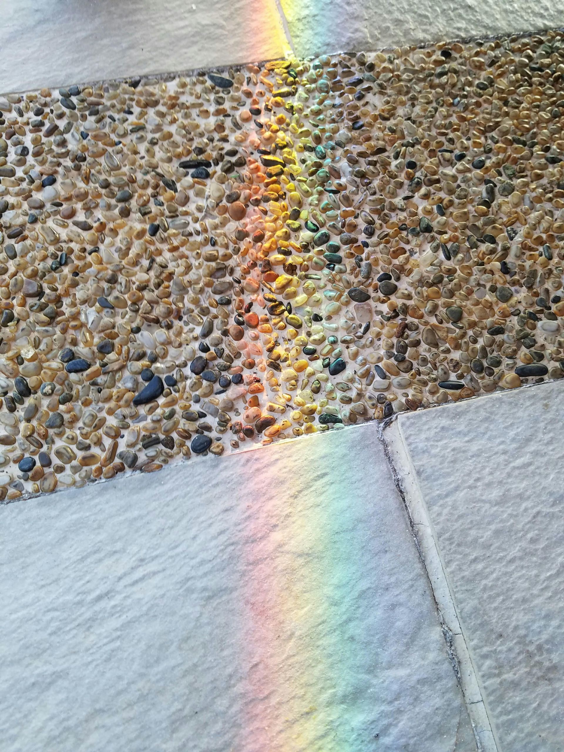 A rainbow is reflected in the rocks on the ground.