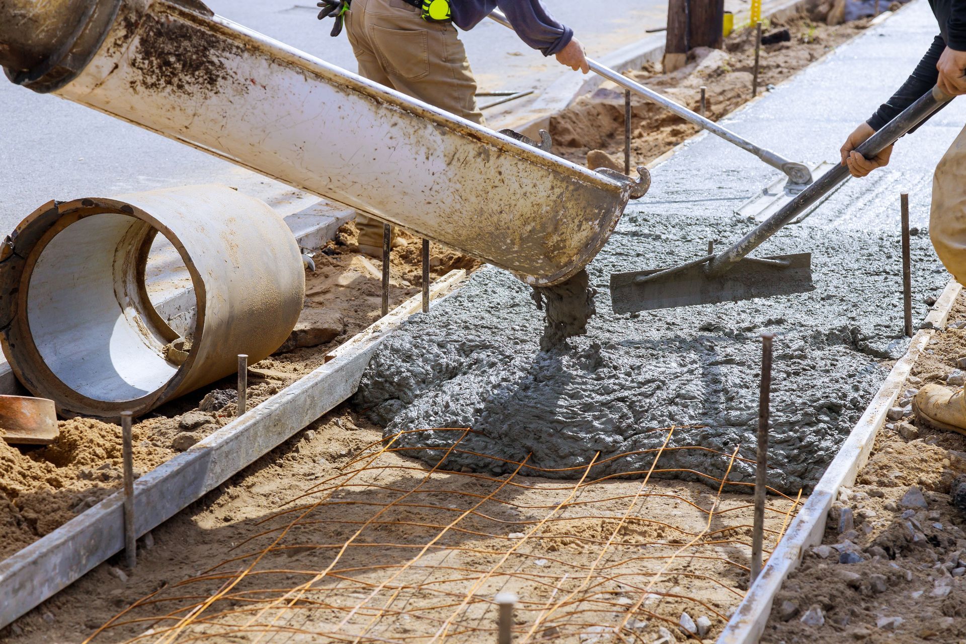 A man is pouring concrete on a sidewalk with a shovel.