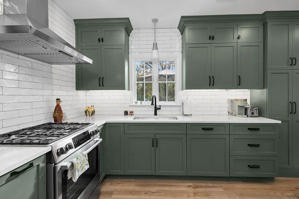Modern kitchen with sage green cabinets, white subway tile, stainless range, and a window over the sink.