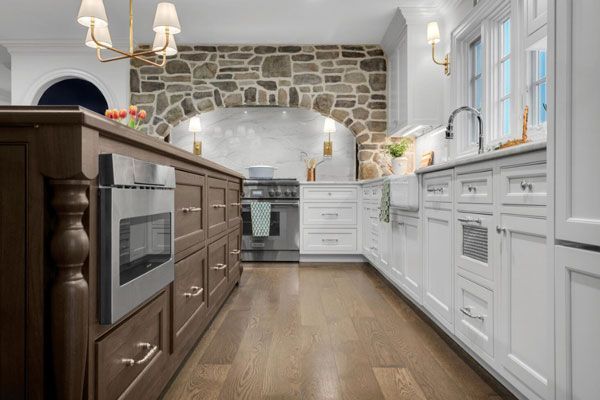 Bright kitchen with white cabinets, dark island, wood floor, and stone accent wall