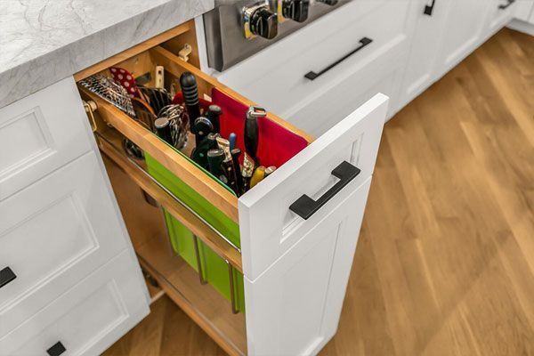 Open kitchen drawer organizer with bottles and wine holders in a white cabinet