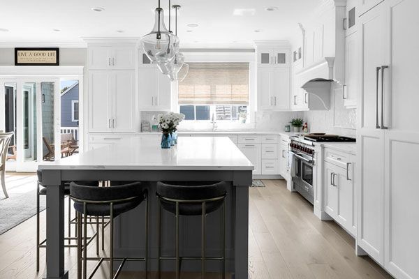 Bright white modern kitchen with a large island, black bar stools, and stainless steel appliances