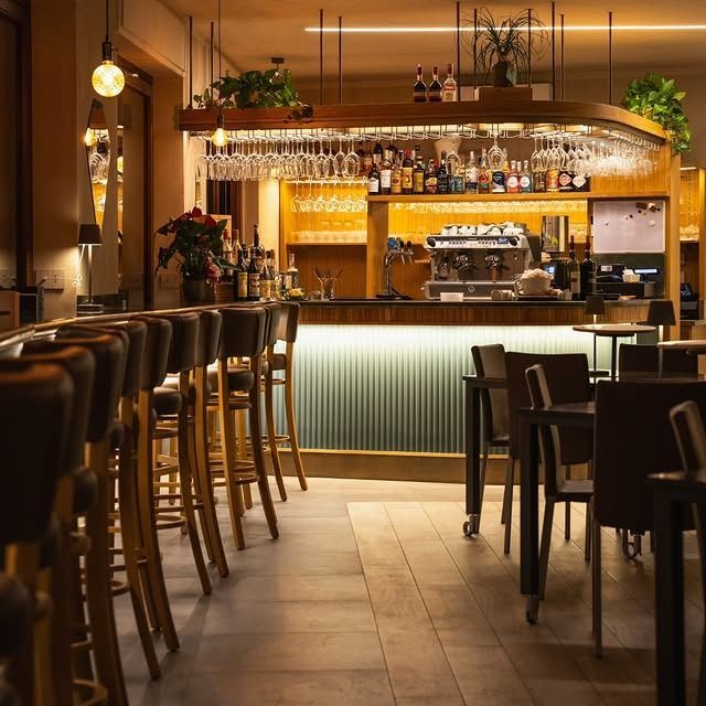 Interno di un elegante bar con sgabelli, tavoli e bancone retroilluminato.