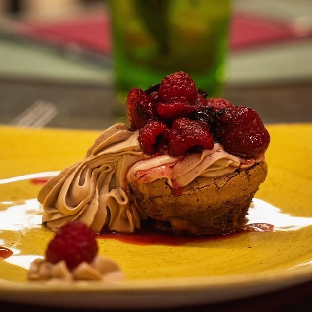 Dessert su piatto giallo: dolcetto al forno con panna montata e lamponi.