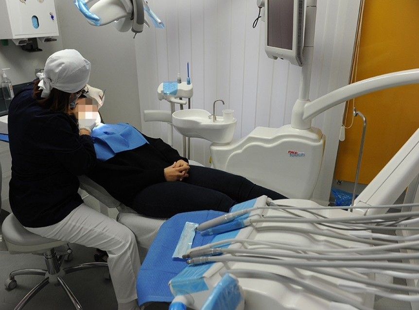 Dentista che visita un paziente su una poltrona. Dentista che indossa cuffia e mascherina. Studio dentistico bianco.