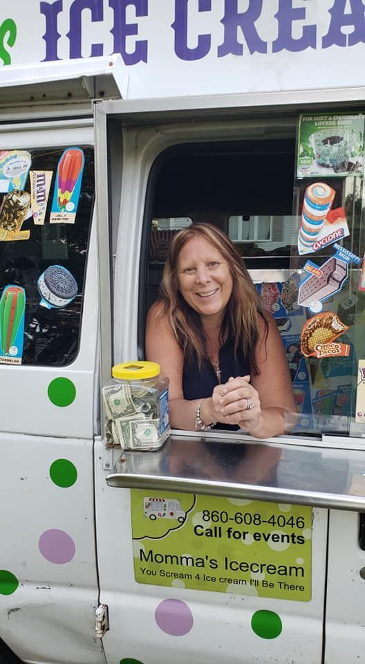 A person smiling through the serving window of a white ice cream truck decorated with colorful polka dots.