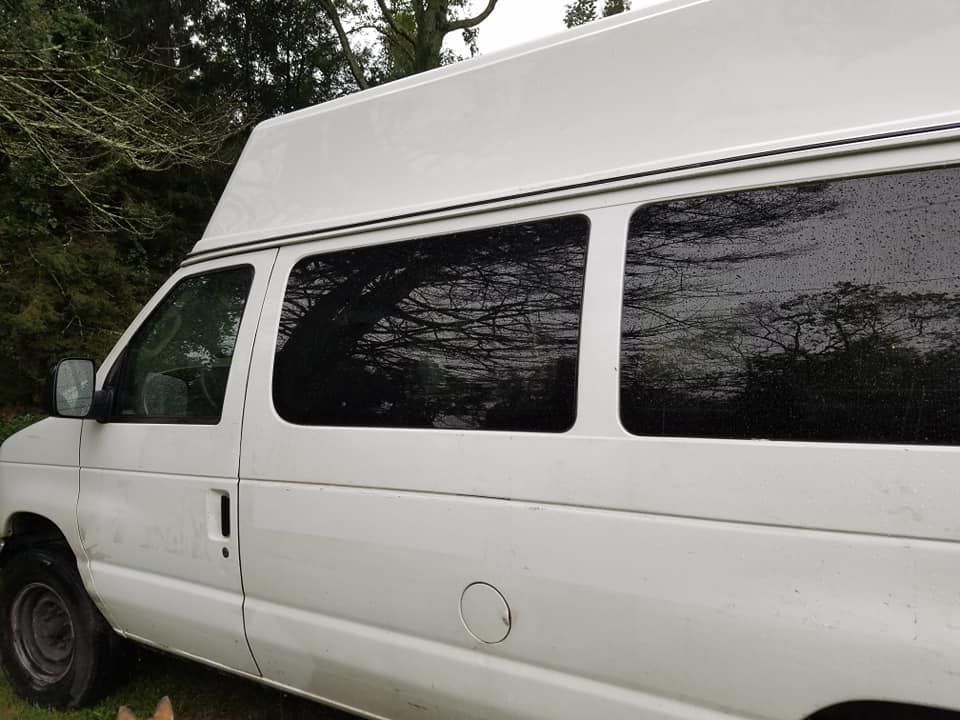 A white high-roof passenger van parked outdoors near trees, viewed from the passenger side.
