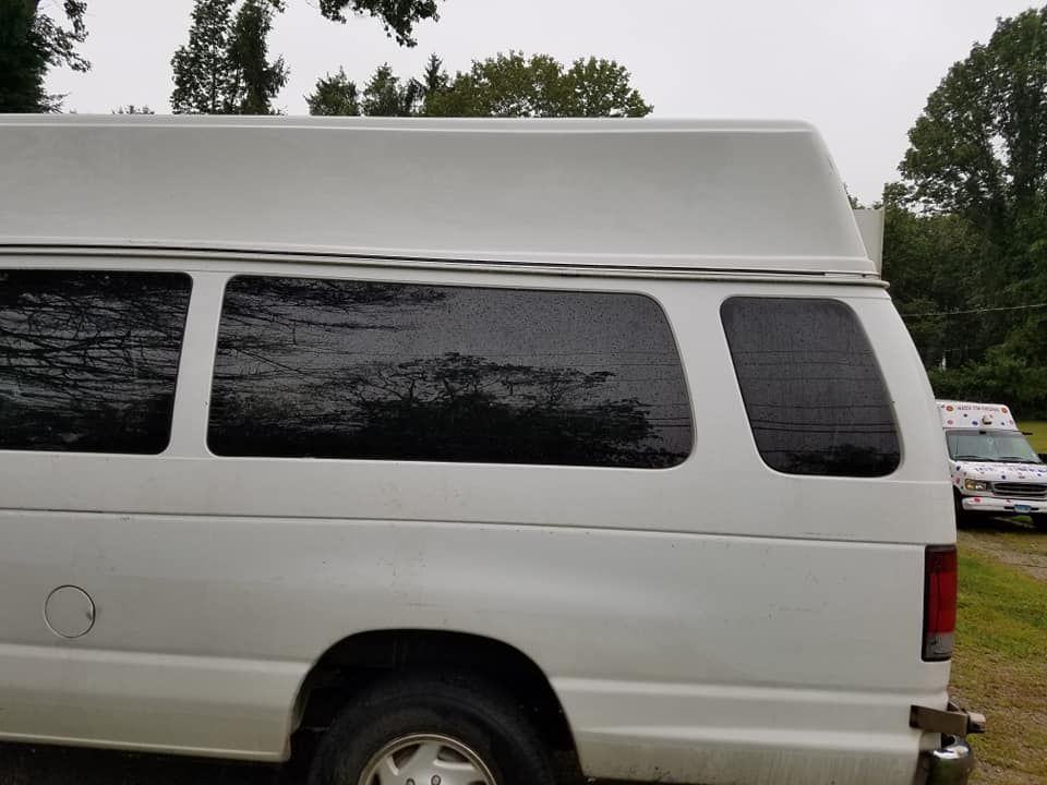 Side view of a white van with a high-top roof, parked outdoors in a grassy area.