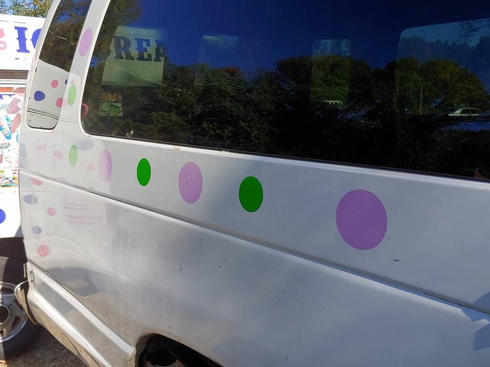 Side view of a white van with decorative, multicolored circles in pink, light green, and blue along its side.