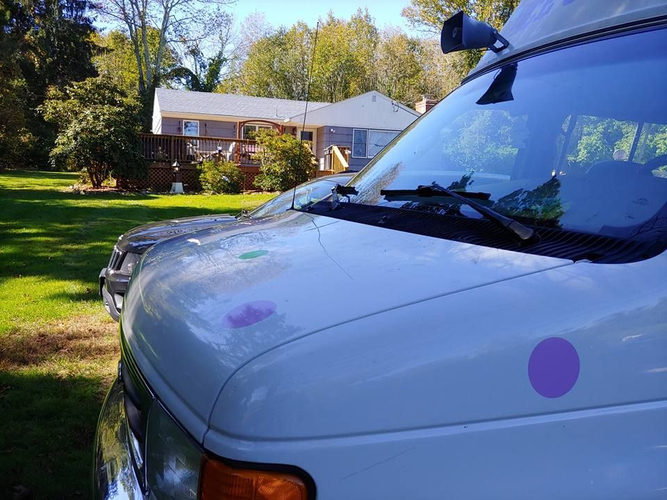 A white van is parked on a lawn in front of a residential house on a sunny day.