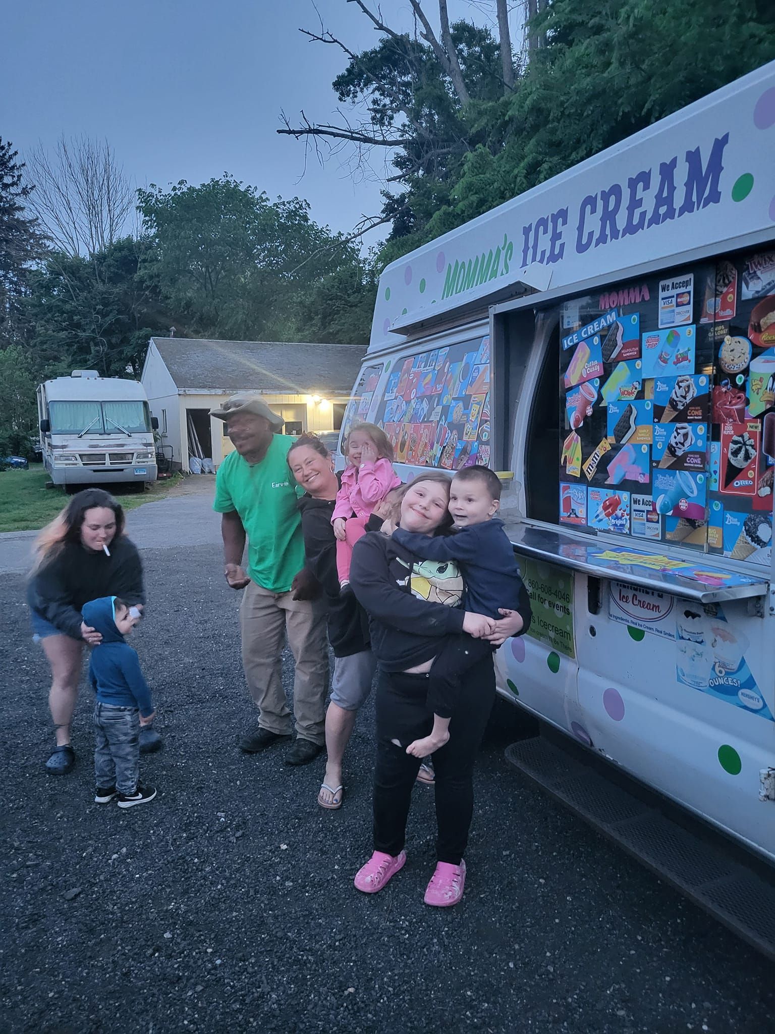 A group of people standing outside an ice cream truck on a gravel lot at dusk.