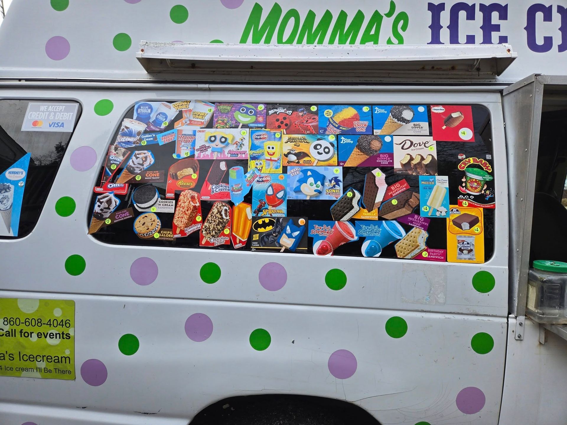 A side view of an ice cream truck with white panels decorated with green and purple polka dots, displaying treat menus.