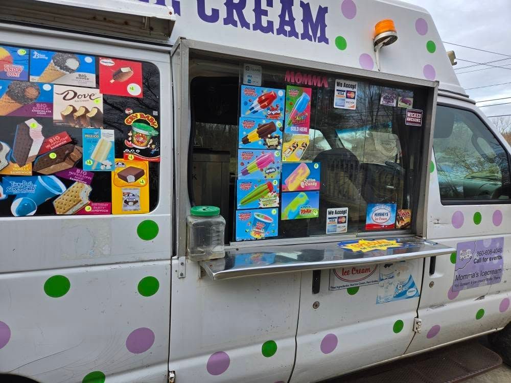 A white ice cream truck with colorful polka dots, featuring a service window displaying a menu of frozen treats.