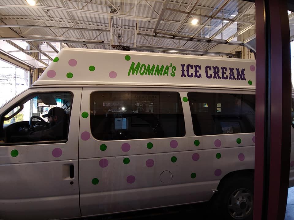A white Momma's Ice Cream van with green and purple polka dots parked indoors under a metal ceiling.