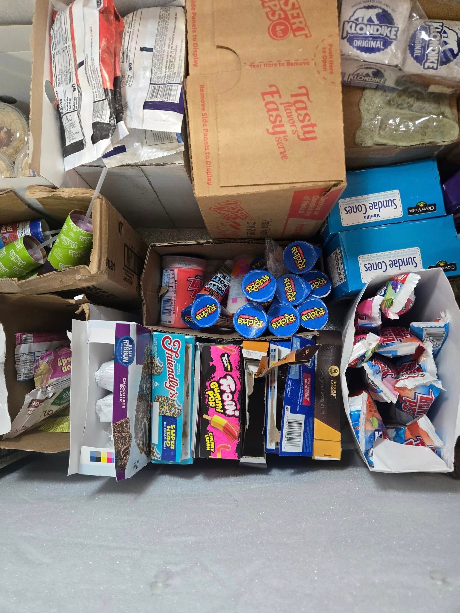 An overhead view of cardboard boxes filled with various packaged snack foods and ice cream products on a flat surface.