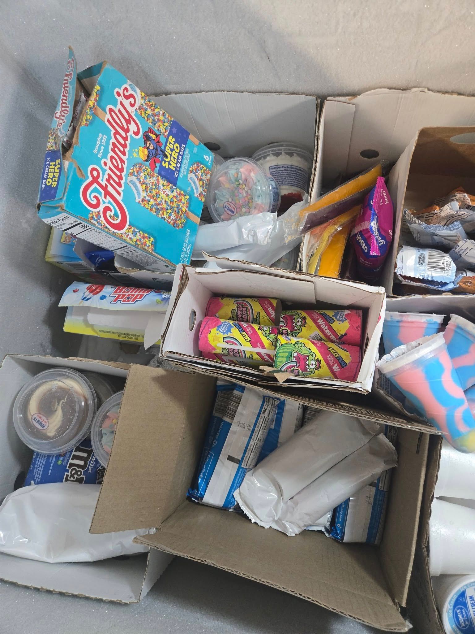 Cardboard boxes filled with assorted snacks, ice cream tubs, and packaged food items.