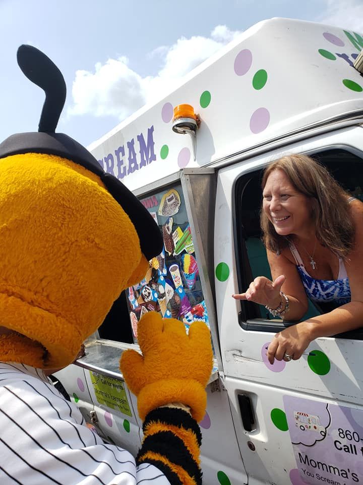 A person in a yellow and black striped mascot costume interacts with a smiling woman leaning out of an ice cream truck.