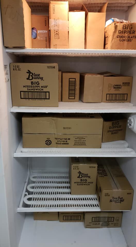 An open, white storage freezer shelf stocked with numerous brown cardboard boxes containing food supplies.