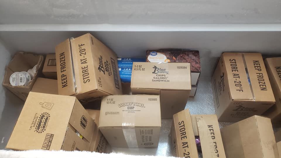 An open chest freezer filled with multiple cardboard boxes of food, with several labels reading