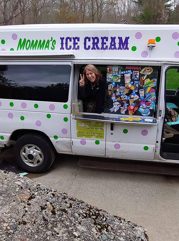 A person making a peace sign from the serving window of a white Momma's Ice Cream truck with colorful polka dots.