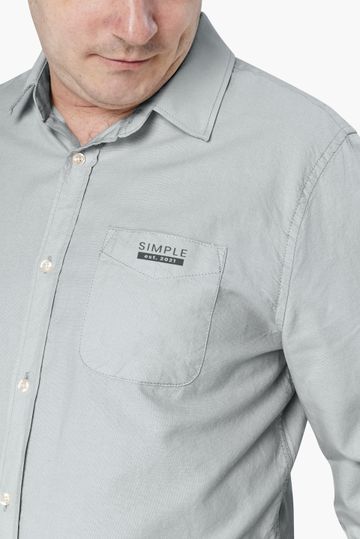 Homem vestindo uma camisa cinza de botões com um bolso pequeno e um logotipo no peito.