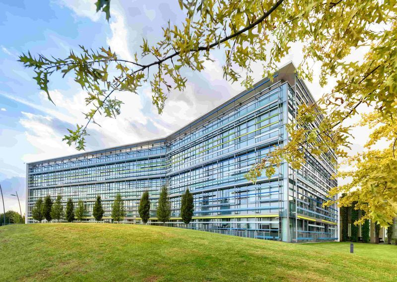 A large building with a lot of windows is surrounded by trees and grass.