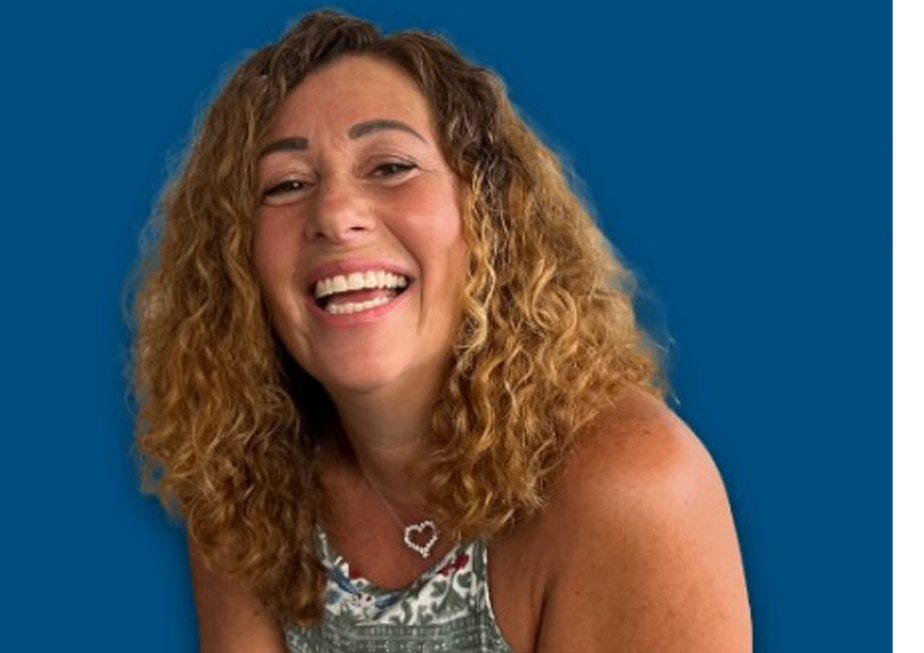A woman with curly hair is smiling and wearing a necklace with hearts on it.