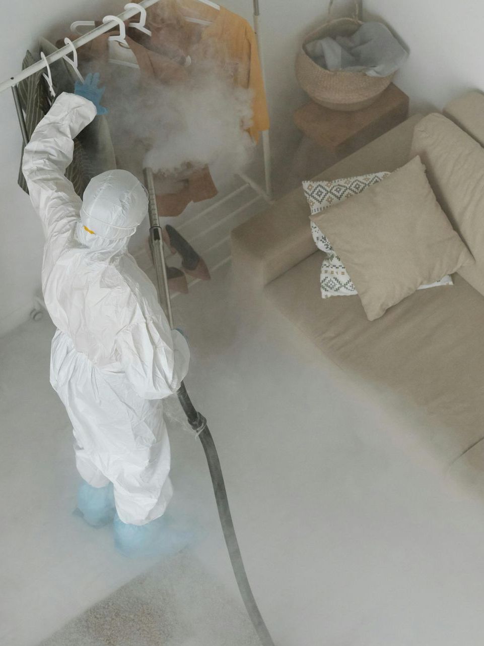 A person in a protective suit is spraying a room with a hose.
