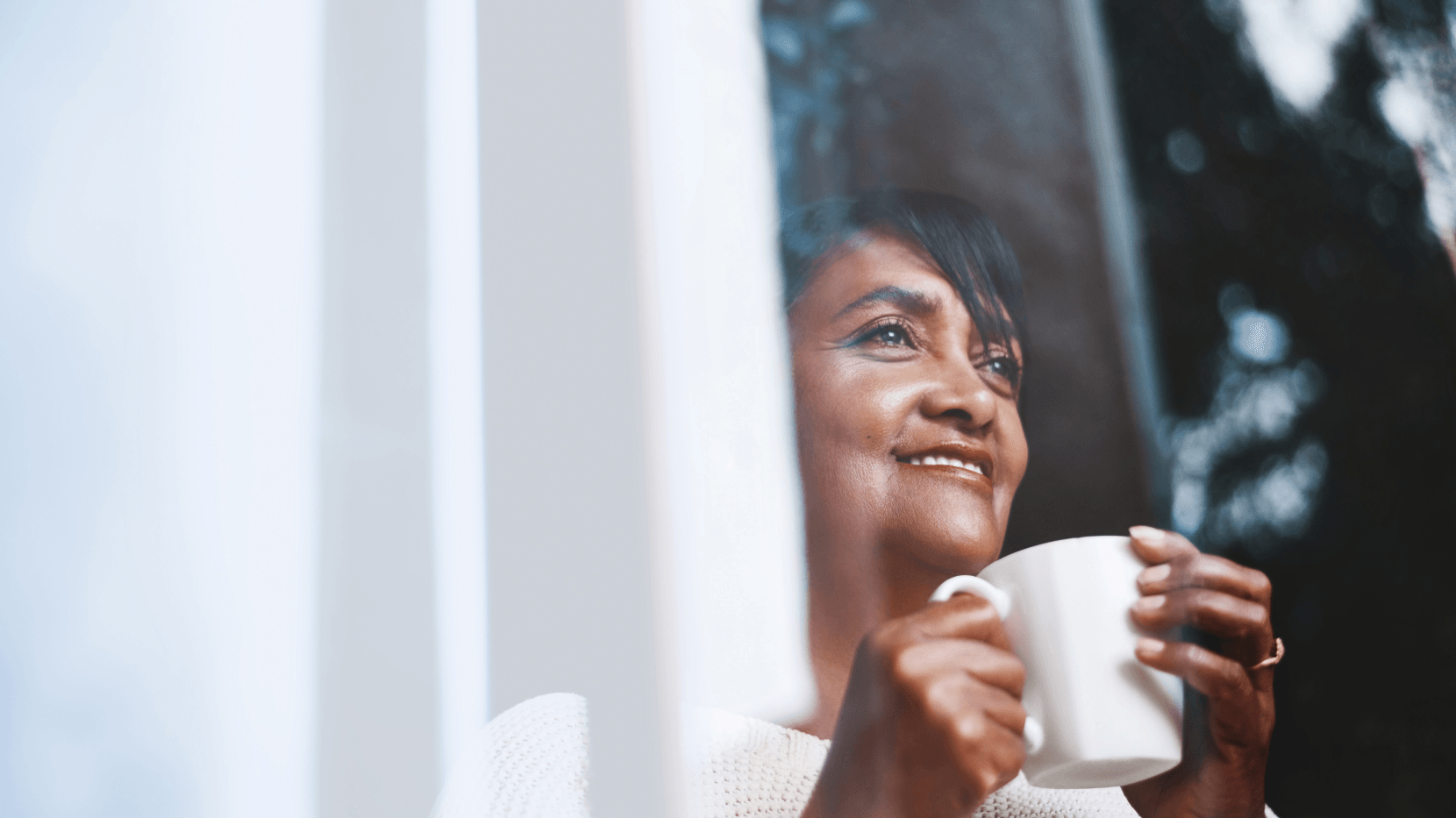 A woman looking out the window and smiling while thinking positively