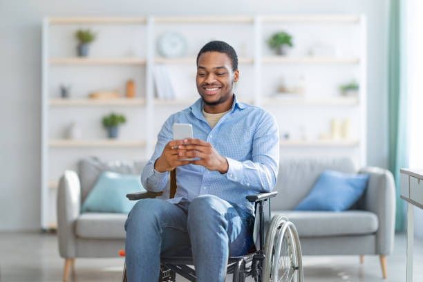 Man in wheelchair smiling at phone in living room.