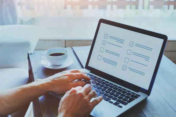 Hands typing on laptop displaying a checklist, coffee cup on table near window.