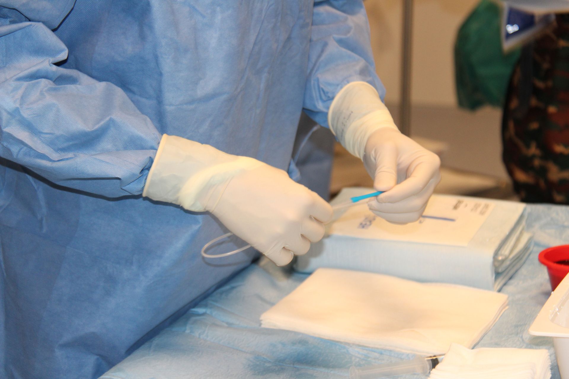 Person in surgical attire prepares medical equipment, holding a small blue tube with gloved hands. Person in surgical attire prepares medical equipment, holding a small blue tube with gloved hands.