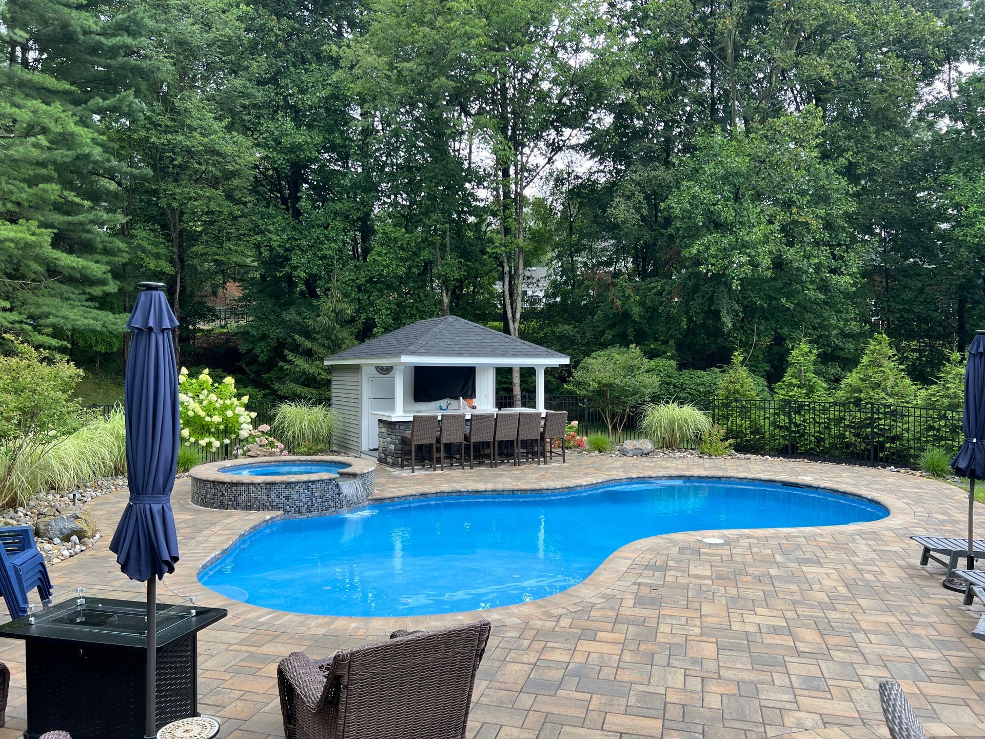 Backyard pool with a bar, hot tub, patio, and lush greenery.
