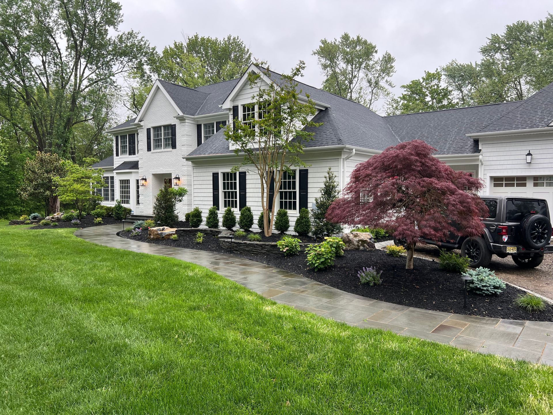 White house with black shutters, lush green lawn, and a red Japanese maple tree in the landscaping.