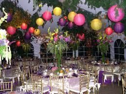 A festive event with colorful lanterns and floral arrangements in a garden setting. Tables are set for a banquet.