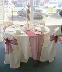 Round table set for a wedding reception with white tablecloth, red runner, and draped chairs.