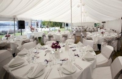 Wedding reception tent with round tables set for guests, white draped ceiling.